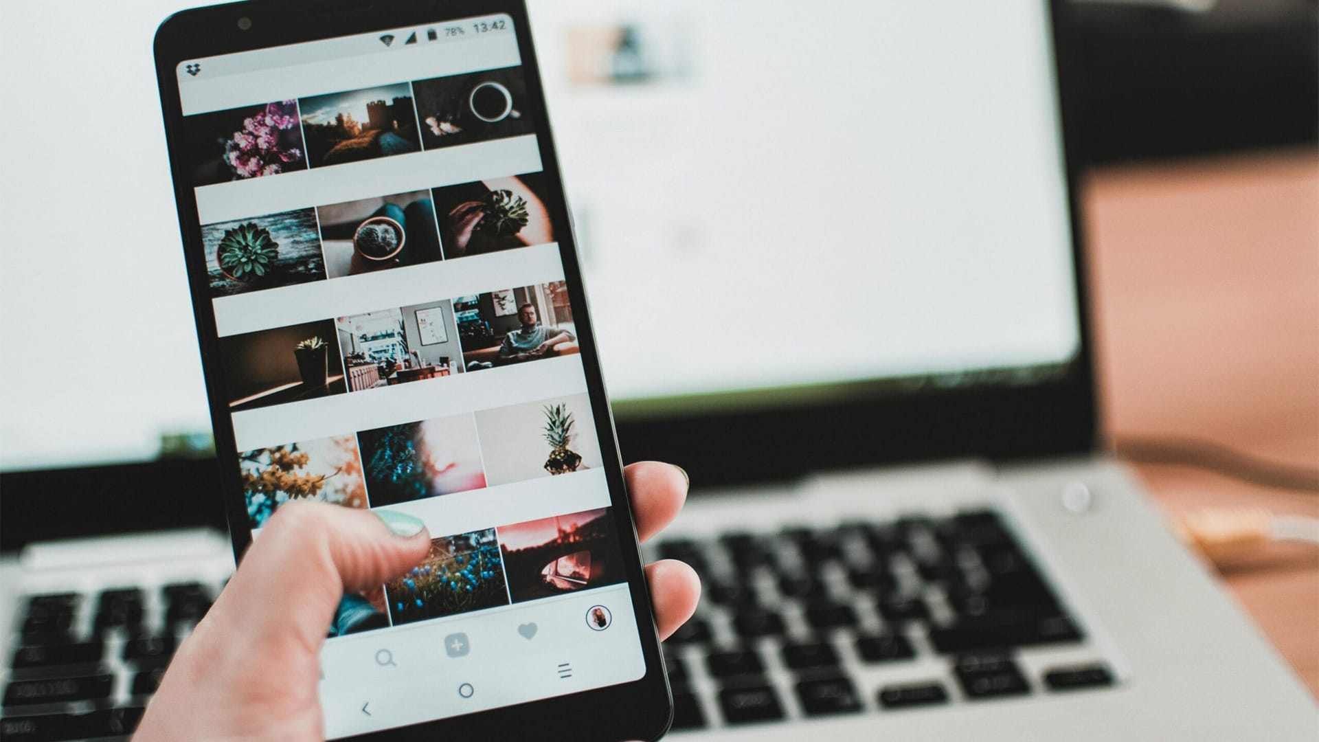 A person uses a smartphone to browse social media in front of a laptop, emphasizing modern technology and lifestyle.