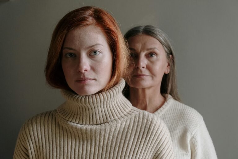 A serene portrait of a mother and daughter in cozy sweaters against a gray background.